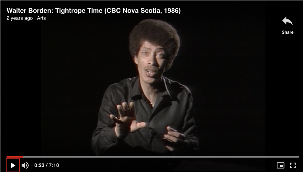 A man in a black shirt with an afro is addressing the camera in mid-speech