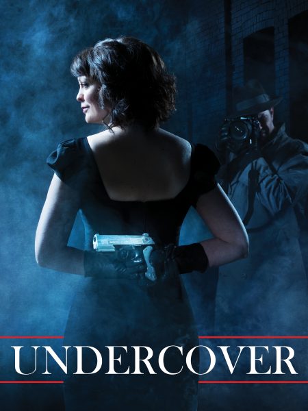 A promotional poster for “Undercover.” The poster has a film noir feel. Rebecca stands with her back to us. She is looking off camera to the left, and her face is illuminated by moonlight. She is holding both hands behind her back, and she is hiding a gun. She is wearing a black dress and a pair of black gloves. There is a man in front of her. He is dressed as a detective, and he is holding a camera up to his eye. At the bottom in large white letters is the title: “Undercover.”