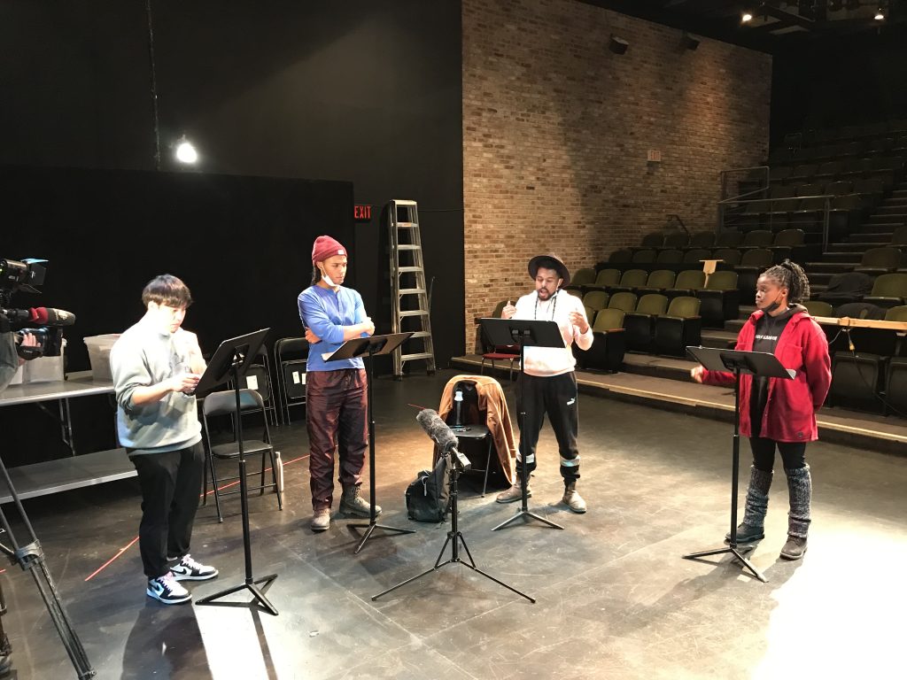 4 actors stand on stage with music stands reading the Vaxx Pass script